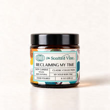 Load image into Gallery viewer, Reclaiming My Time 8 oz soy candle in amber glass jar with Classic Collection label on ivory background